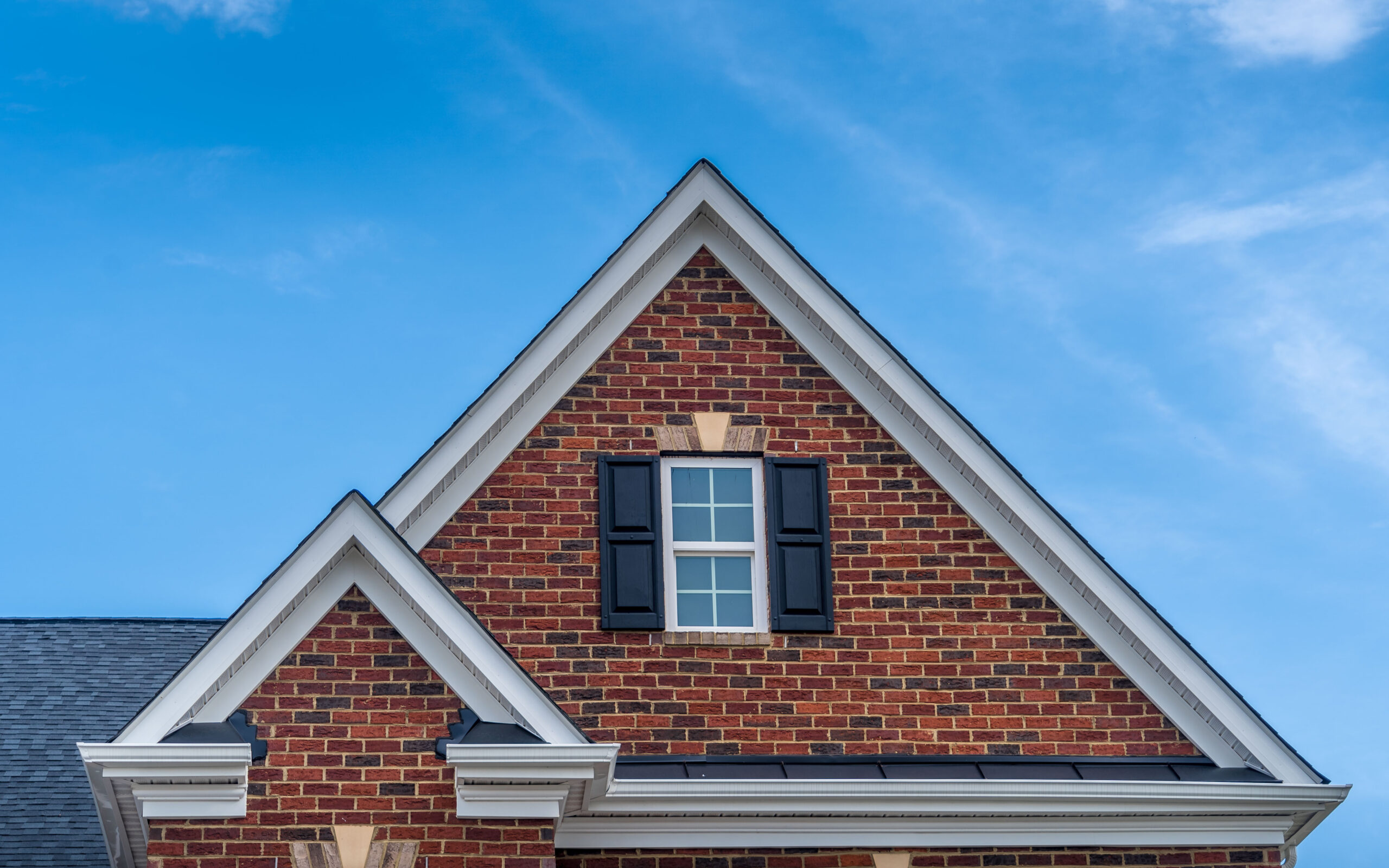 Double hip-to-gable conversions with red brick facade siding, double-hung window with white frame, vinyl shutters on a pitched roof attic